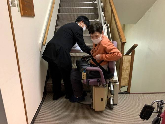 貸切風呂へ向かう階段に設置されている昇降機に座った母とシートベルト装着を手伝ってくれているスタッフ