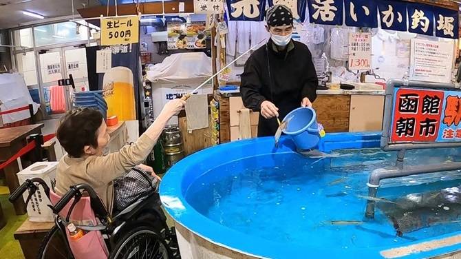 函館朝の市・駅二市場のイカ釣り堀で車椅子でイカ釣り　イカを引き揚げるところ
